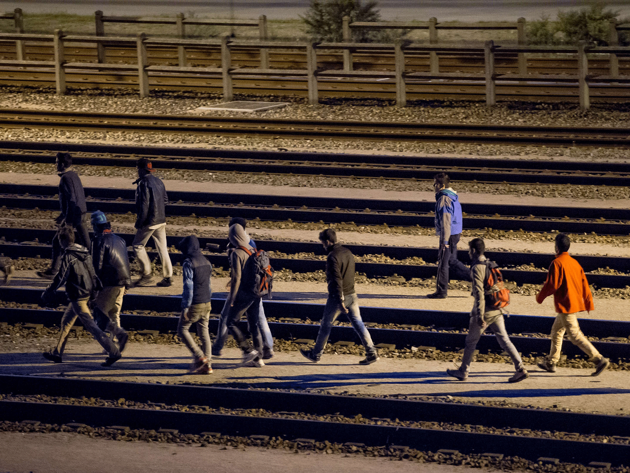 Migrants walk along railway tracks at the Eurotunnel terminal on July 28, 2015 in Calais-Frethun