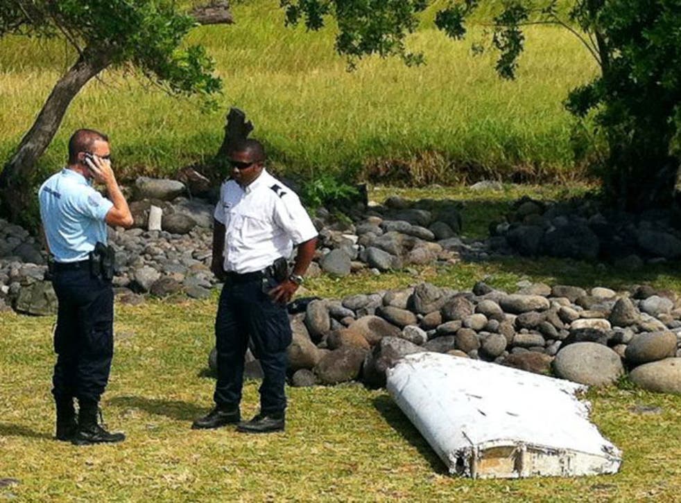 A policeman and a gendarme stand next to a piece of debris from an unidentified aircraft found in the coastal area of Saint-Andre de la Reunion, in the east of the French Indian Ocean island of La Reunion.