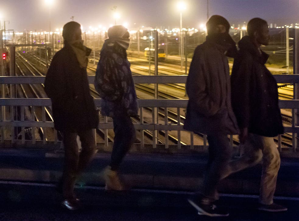 Migrants crossing a bridge over the railway tracks of the Eurotunnel terminal in Calais