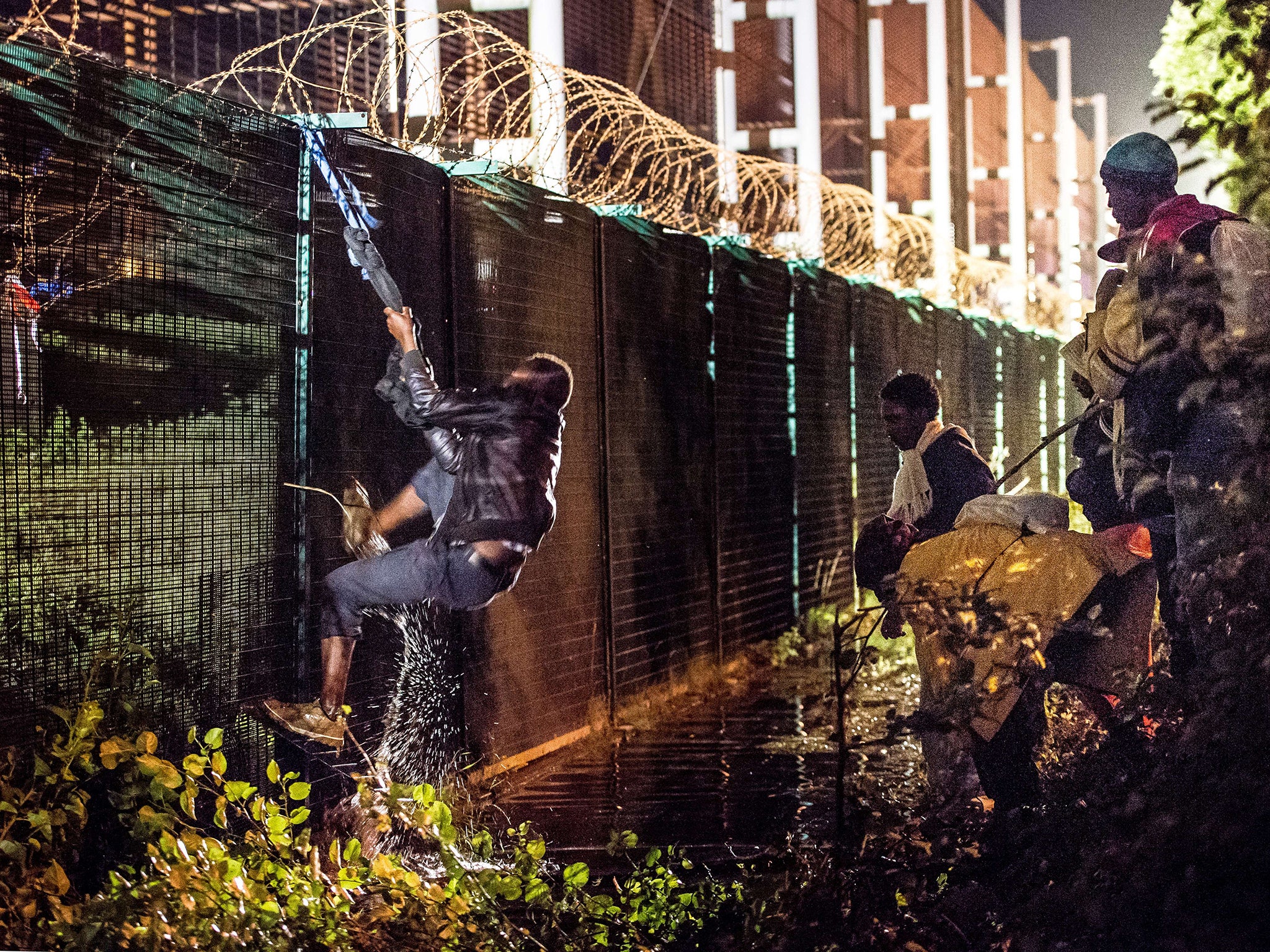 A migrant climbs a security fence of a Eurotunnel terminal in Coquelles near Calais