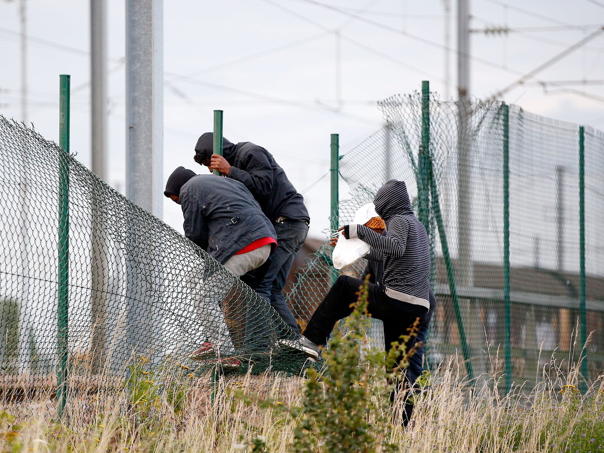 Migrants step over the fence as they try to catch a train to reach England, in Calais