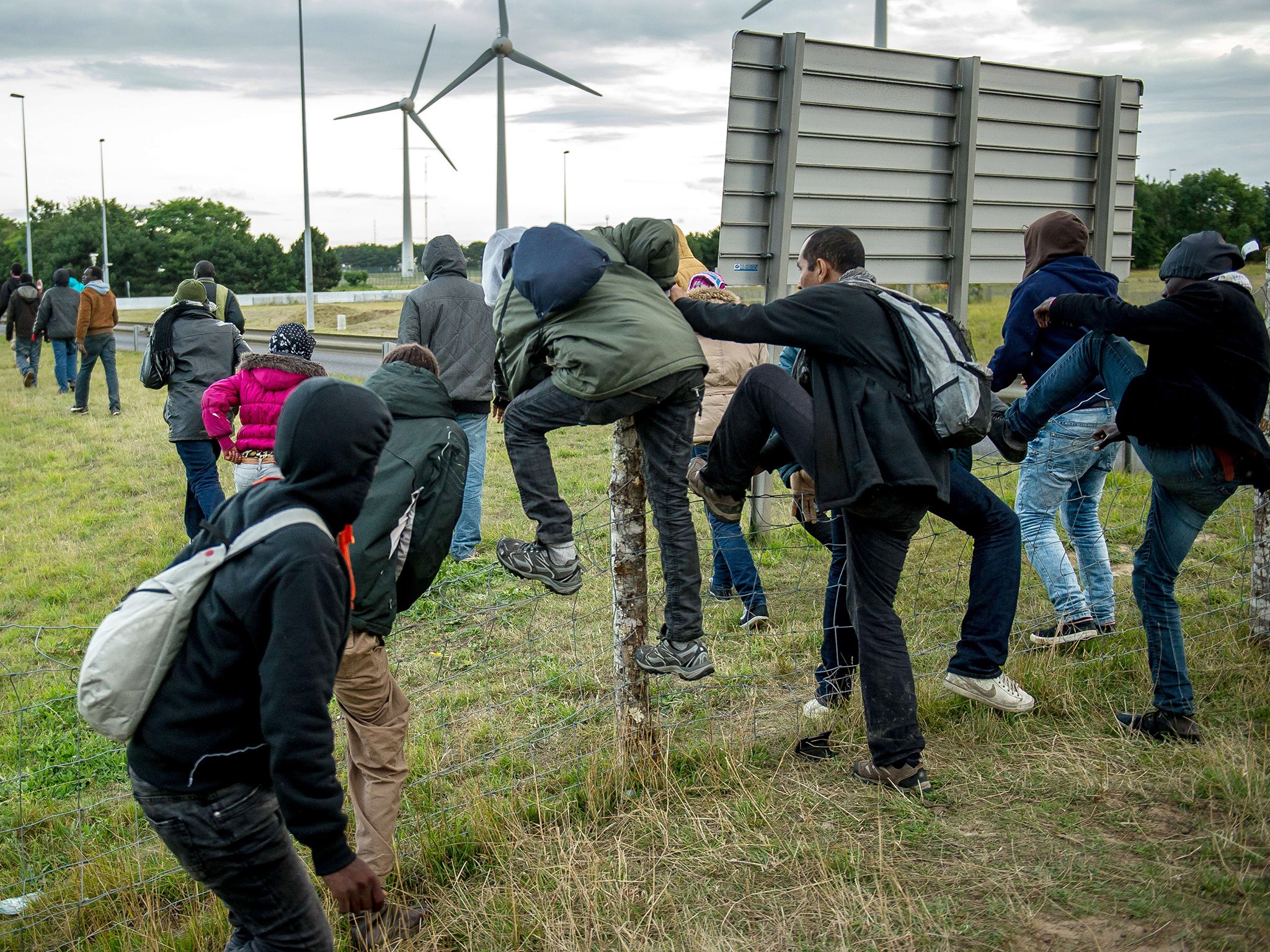 Migrants who managed to pass the police block on the Eurotunnel site climb over a fence to make their way towards the boarding docks in Coquelles near Calais