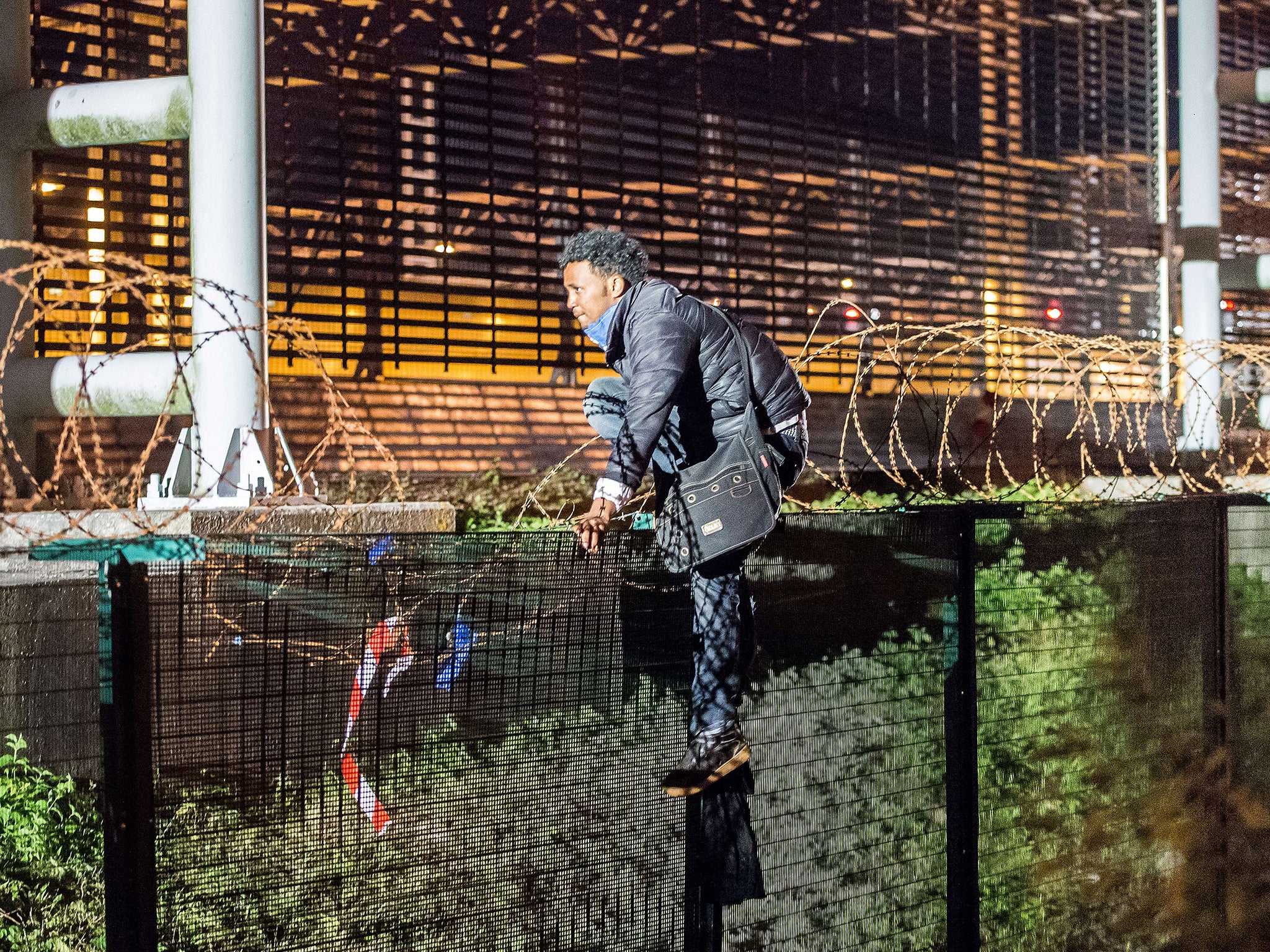 A migrant climbs a security fence of a Eurotunnel terminal in Coquelles near Calais
