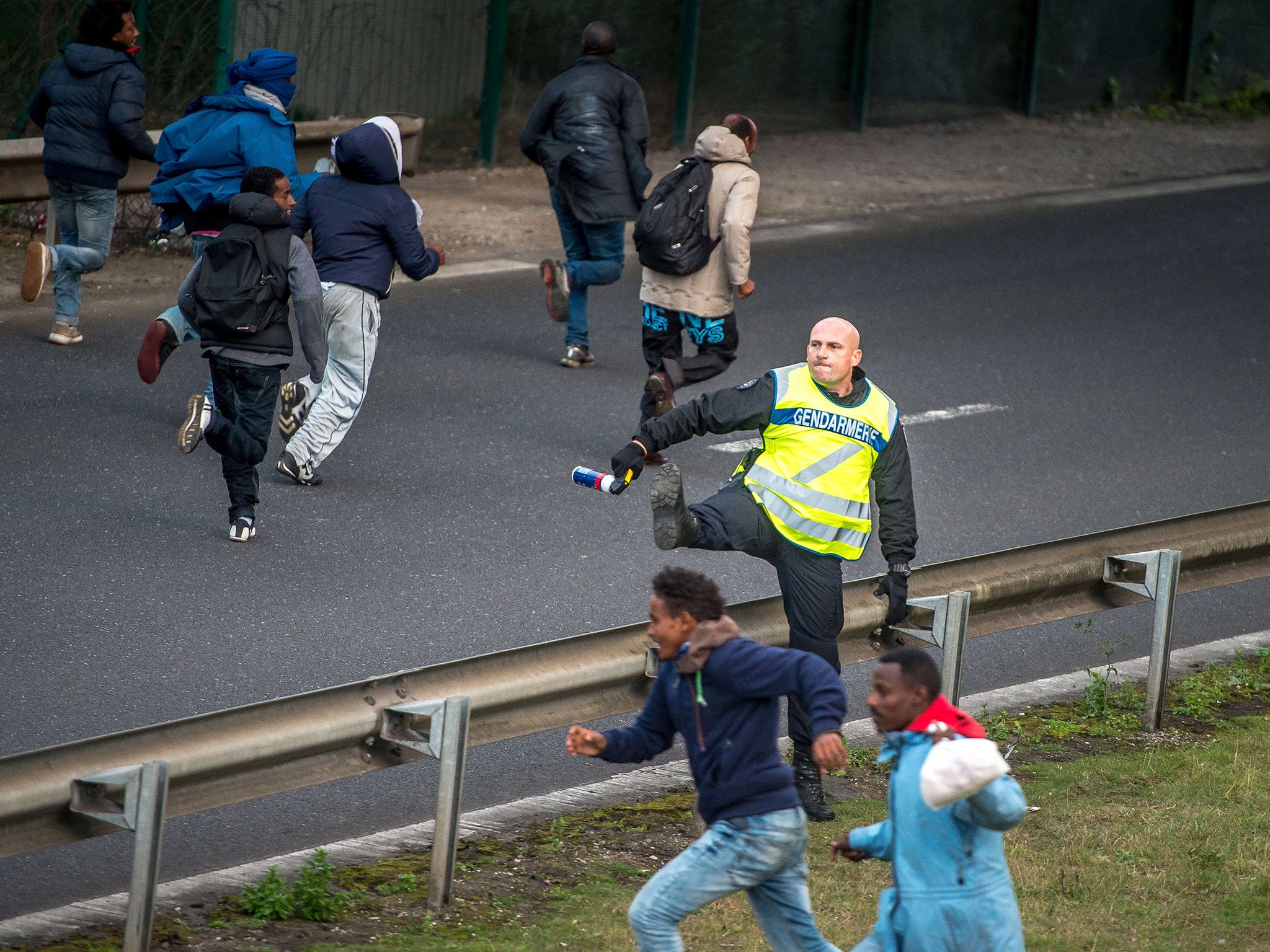 A policeman tries to stop migrants on the Eurotunnel site in Coquelles near Calais