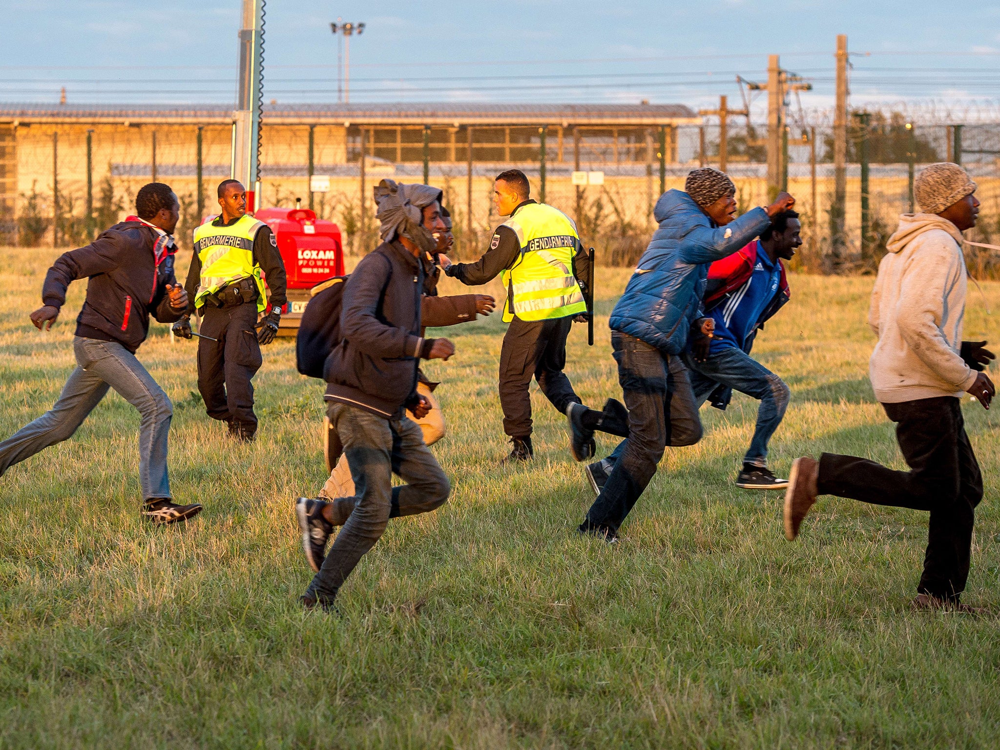 Migrants trying to reach the Channel Tunnel run past policemen in Coquelles near Calaisa