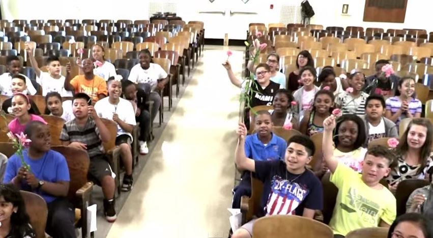 Pupils held-up pink carnations as a way of letting the teacher know she is not alone in her battle (via YouTube)