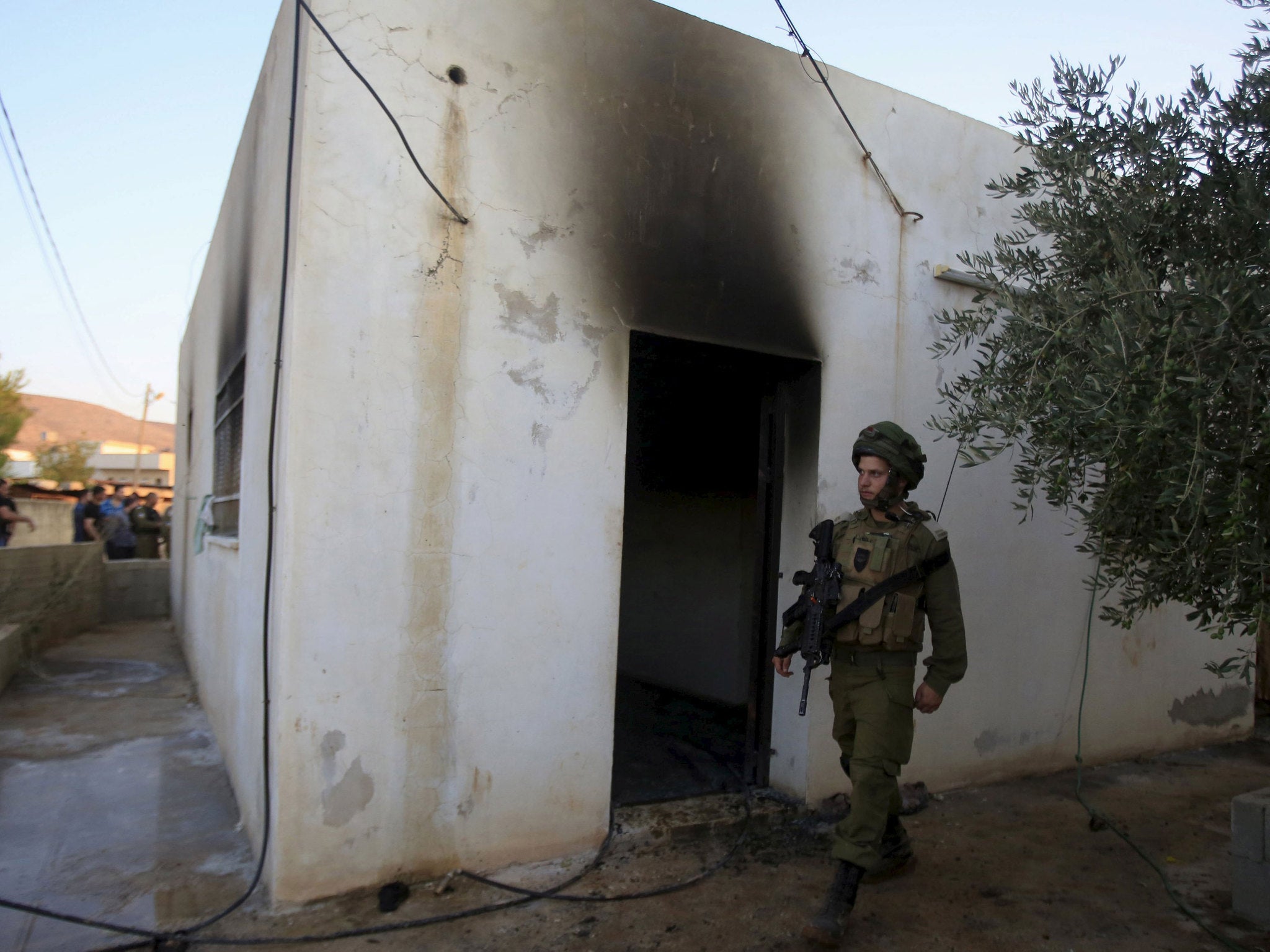 An Israeli soldier walks past a house that had been torched in a suspected attack by Jewish extremists