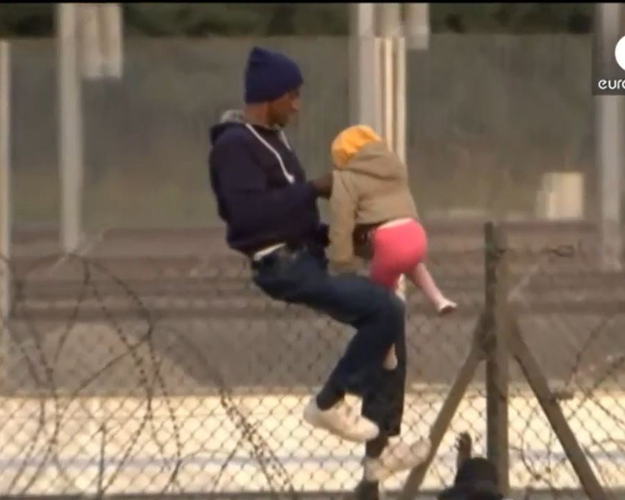 A man is seen lifting a small child over the fence at Calais