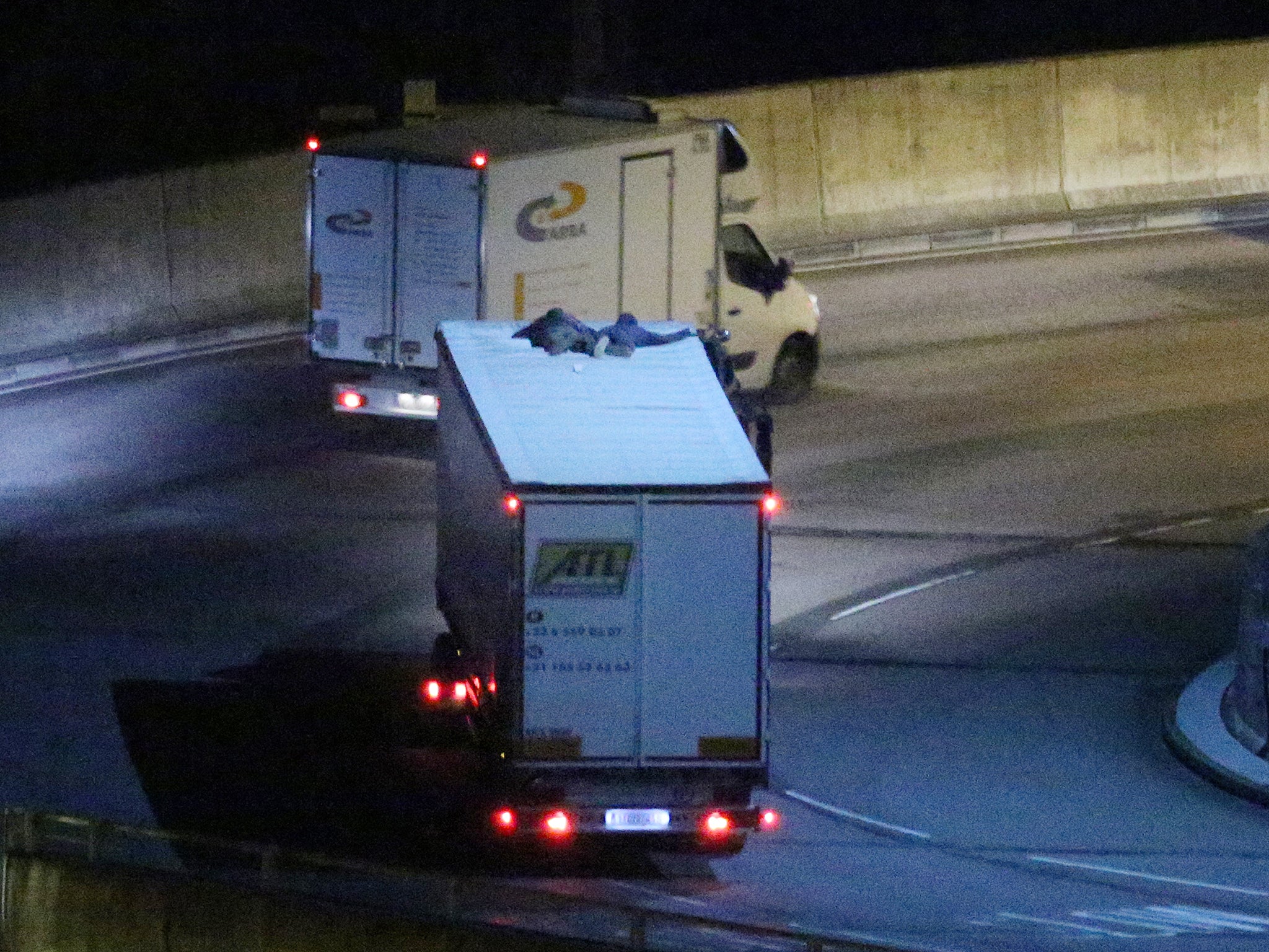 Two migrants cling to the roof of a freight truck as it leaves the Eurotunnel terminal in Folkestone