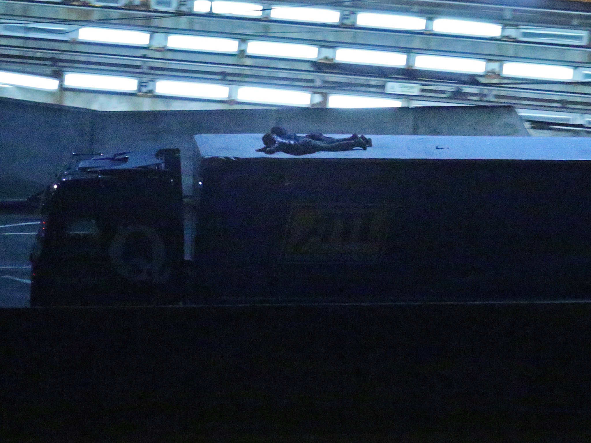 Two migrants cling to the roof of a freight truck as it leaves the Eurotunnel terminal in Folkestone