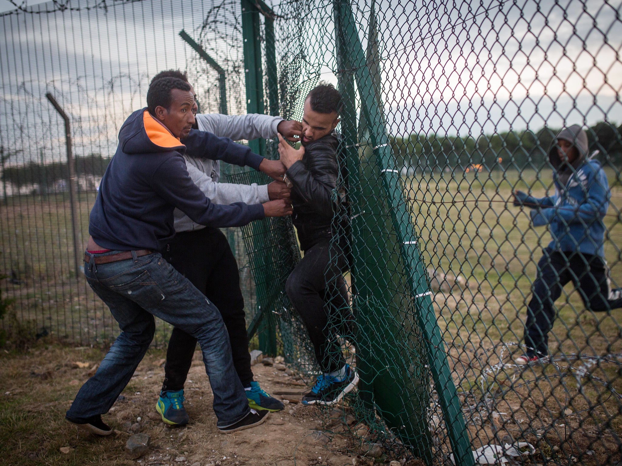 Migrants help a man squeeze through a gap in a fence near the Eurotunnel terminal in Coquelles in Calais