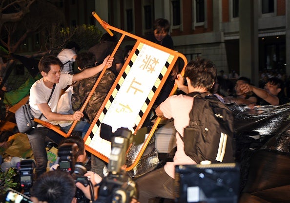 Protesters use a barricade to push down a barbed wire fence as they cross over into the ministry (via SAM YEH/AFP/Getty Images)