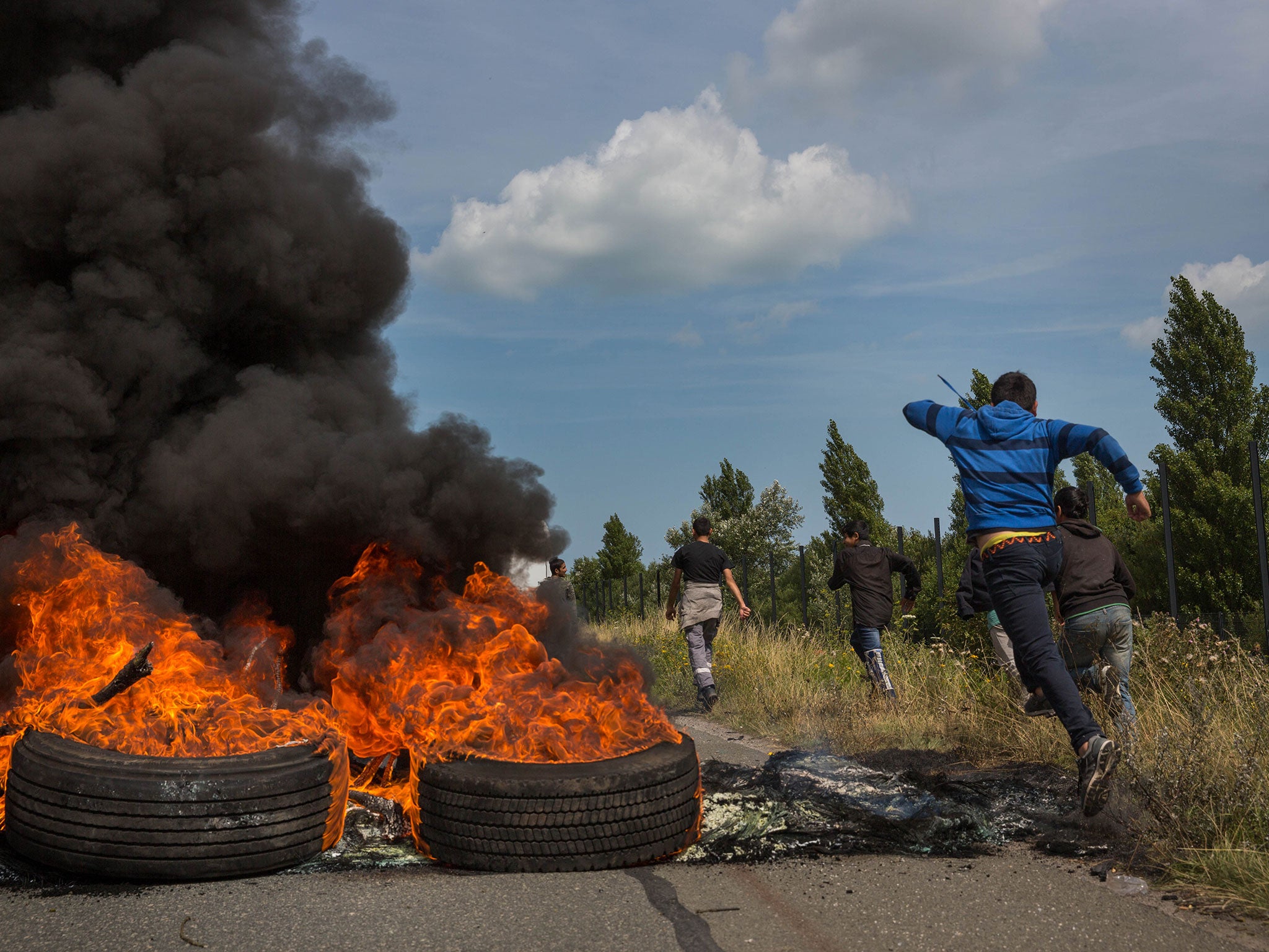 People run past tyres burning on a road leading to the port of Calais on July 31, 2015 in Calais (Getty)