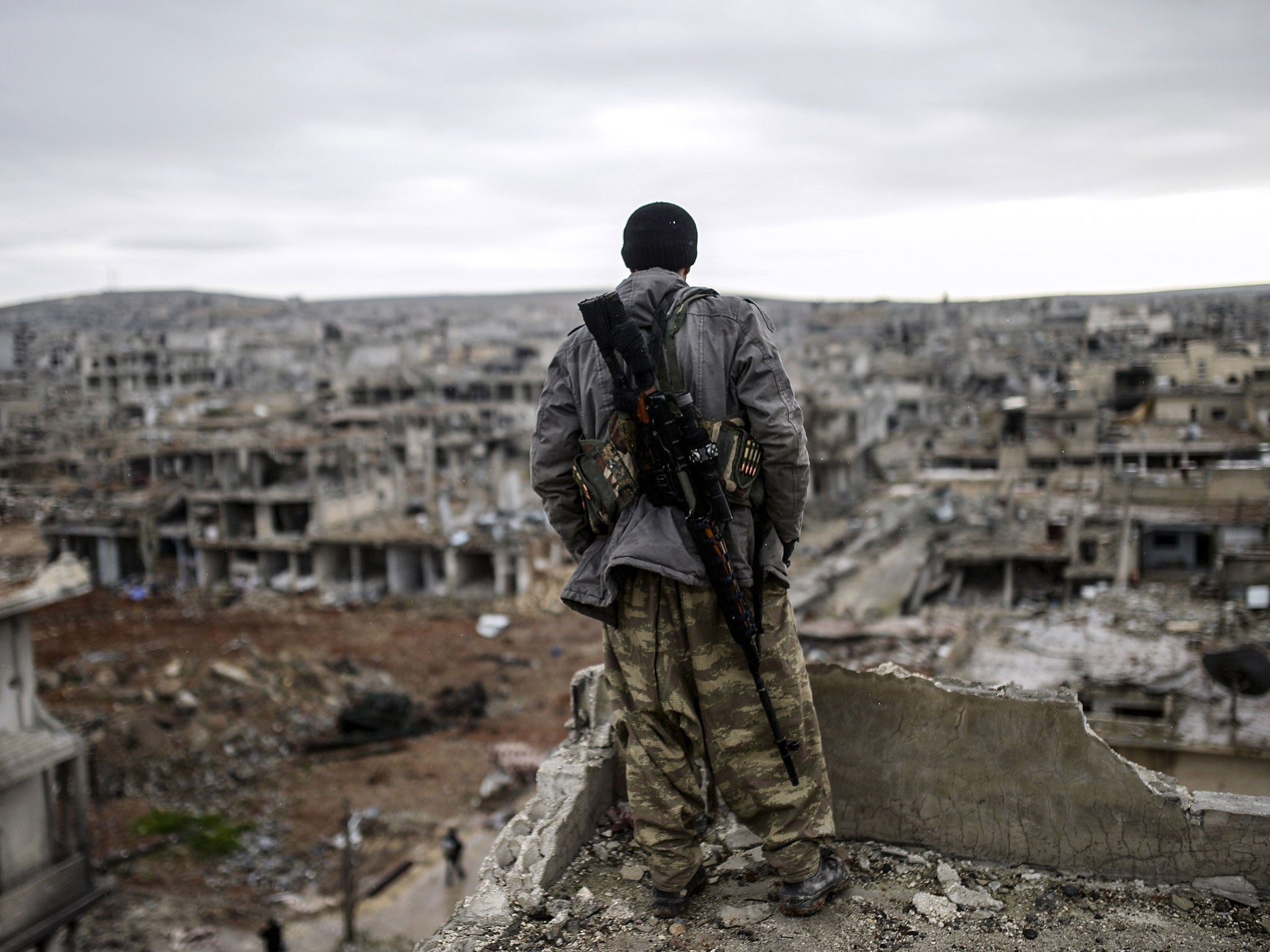 Musa, a 25-year-old Kurdish marksman, stands atop a building as he looks at the destroyed Syrian town of Kobane