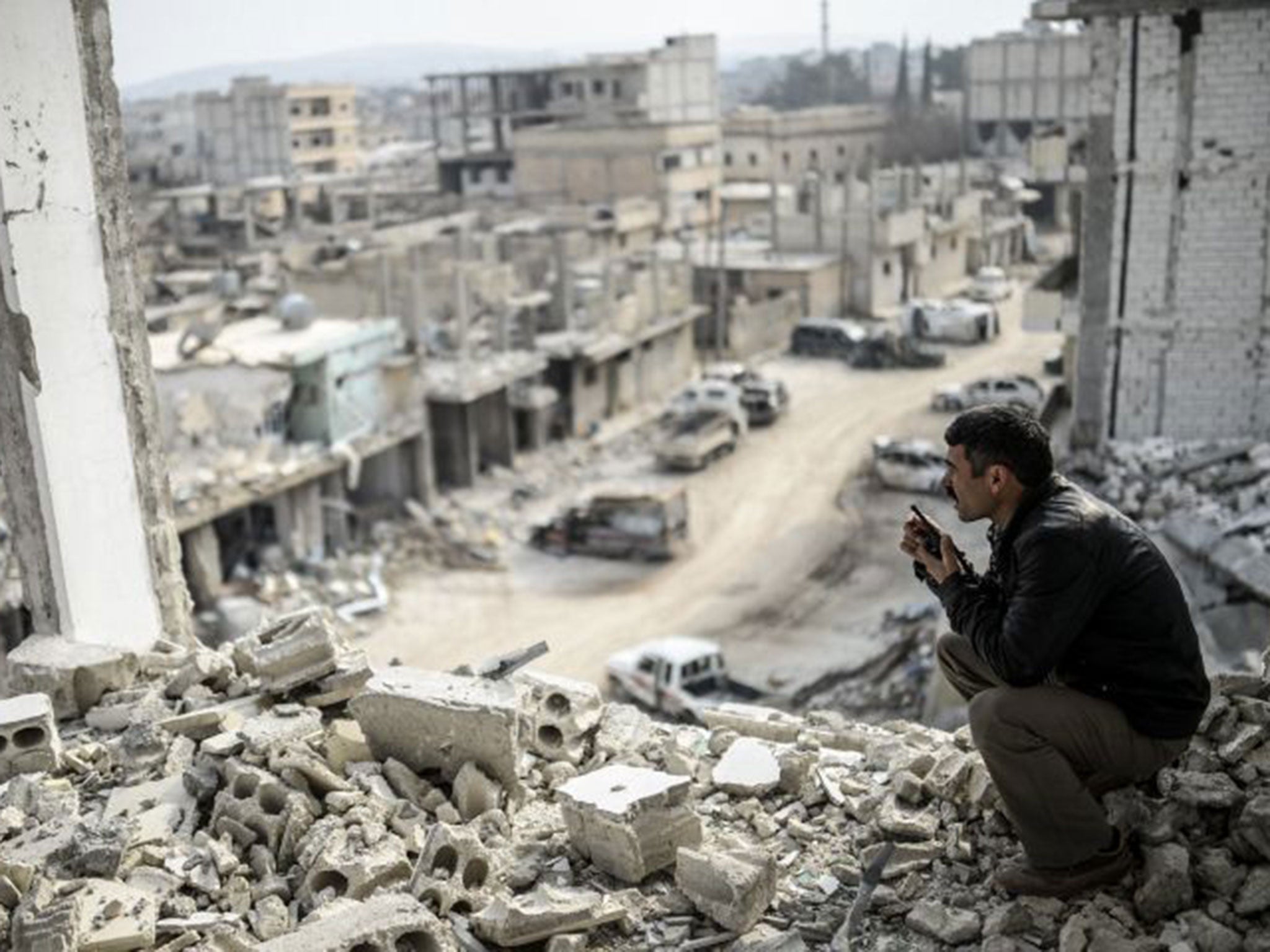 A Kurdish man talks with a radio as he checks the eastern part of the Syrian border town of Kobane