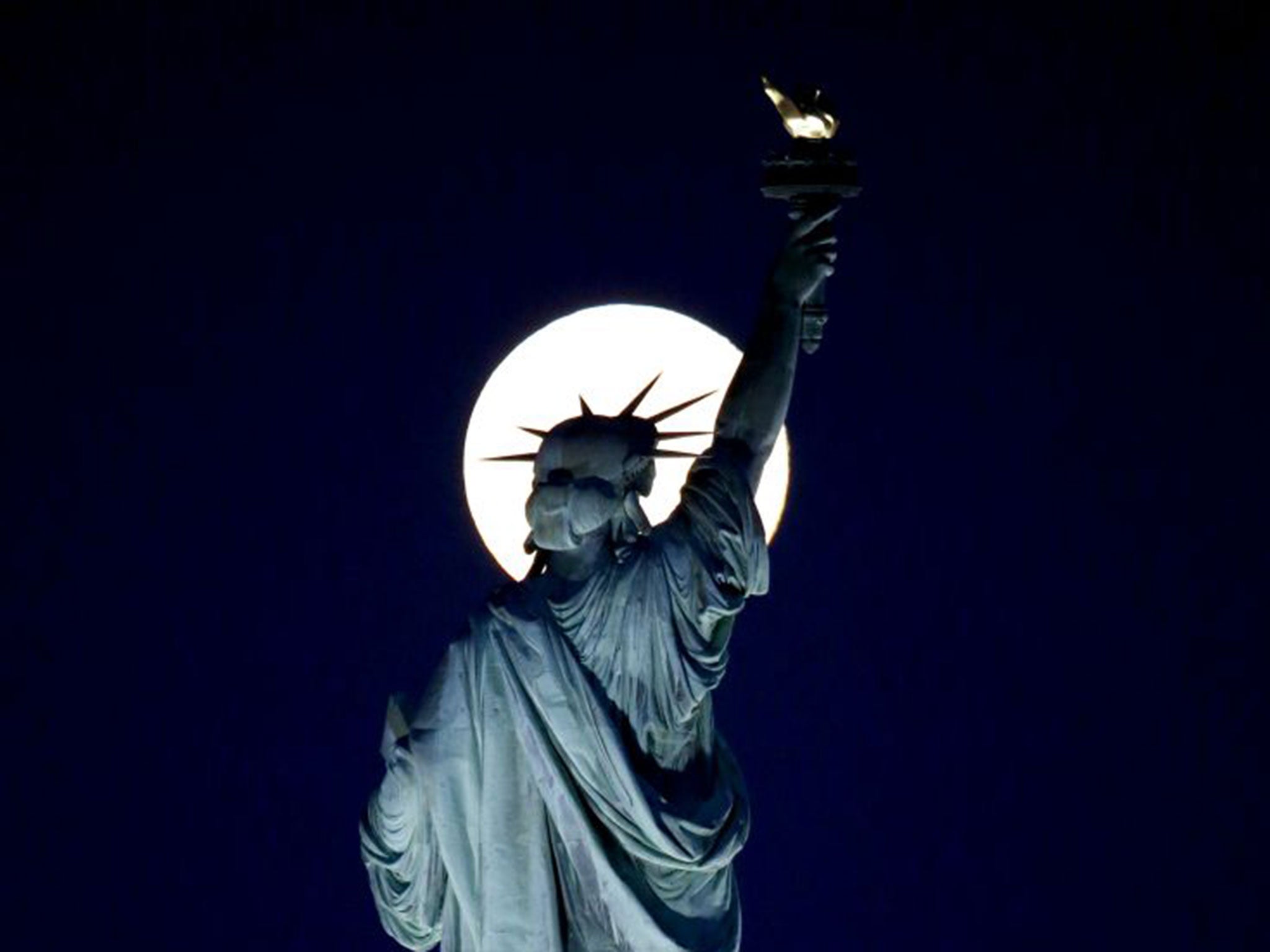 A blue moon rises behind the torch of the Statue of Liberty seen from Liberty State Park in Jersey