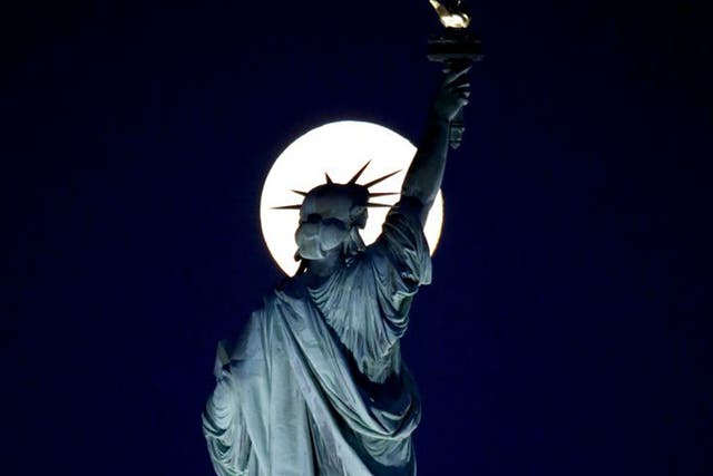 A blue moon rises behind the torch of the Statue of Liberty seen from Liberty State Park in Jersey 