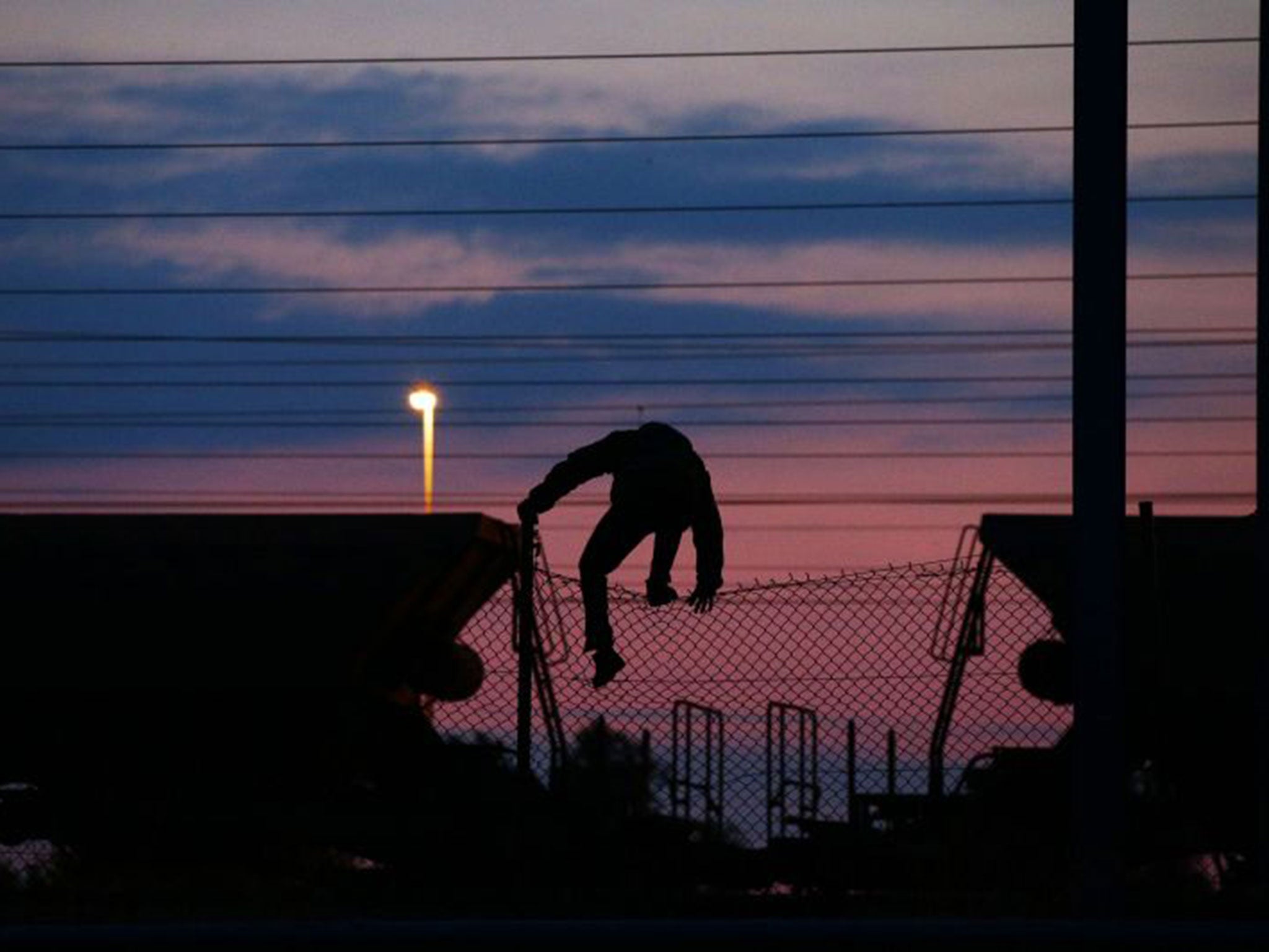 A migrant climbs over a fence on to the tracks near the Eurotunnel site at Coquelles in Calais, France