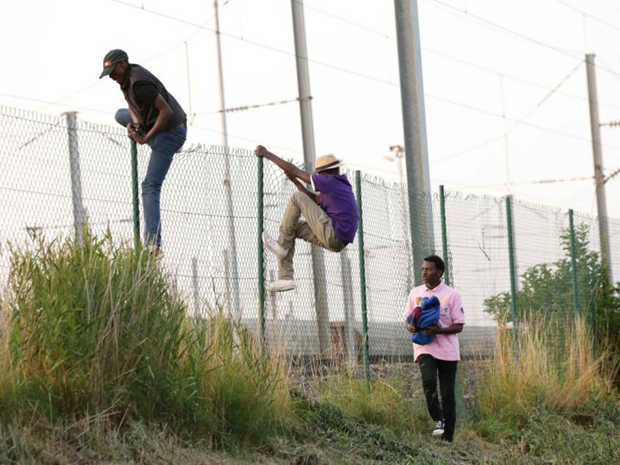 Migrants climb over a fence onto the tracks near the Eurotunnel site at Coquelles in Calais (PA)