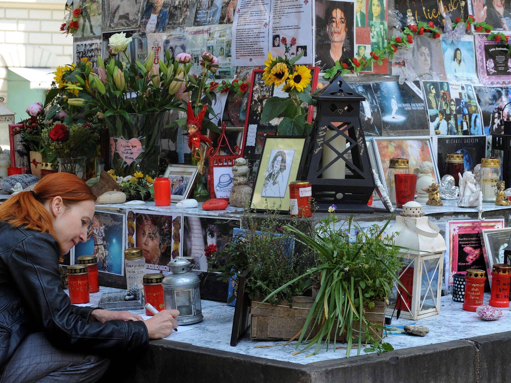 A woman kneels beside flowers, letters and pictures of the King of Pop Michael Jackson which are fixed on a monument dedicated to Franco-Flemish Renaissance composer Orlando di Lasso in Munich