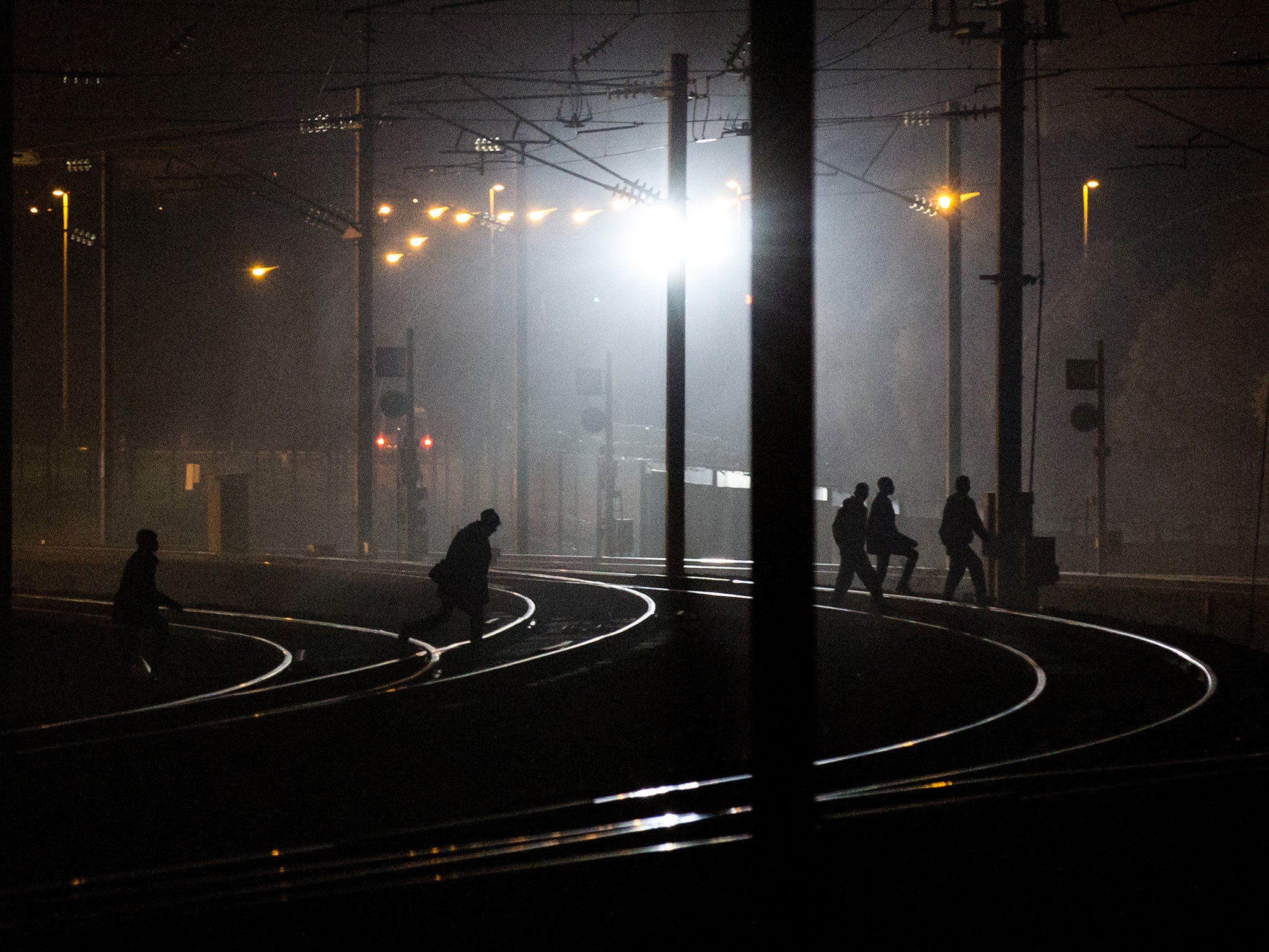 People walk across train tracks near the Eurotunnel terminal in Coquelles on August 3, 2015 in Calais, France