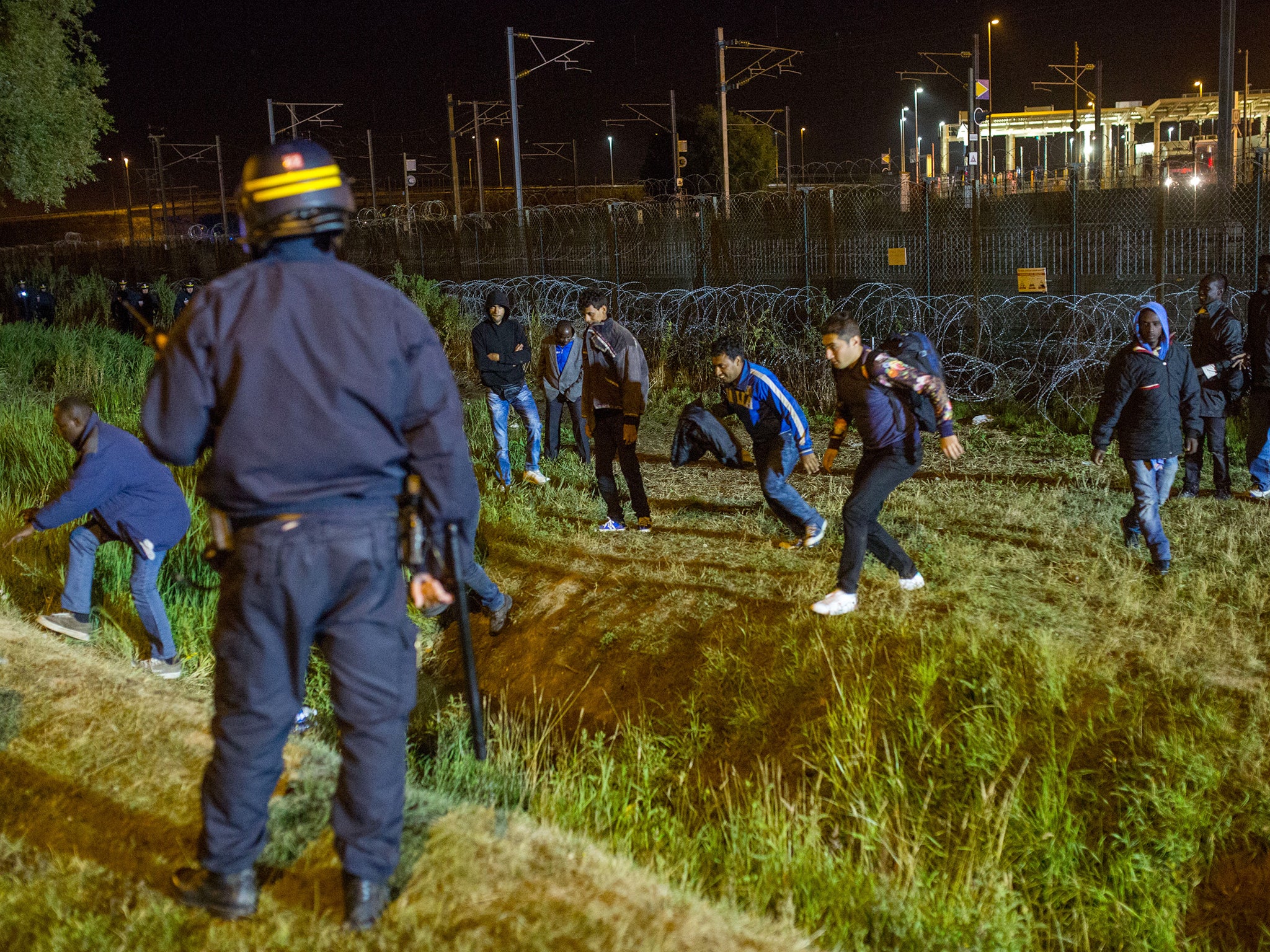 A policeman watches men move away from a security fence beside train tracks near the Eurotunnel terminal in Coquelles