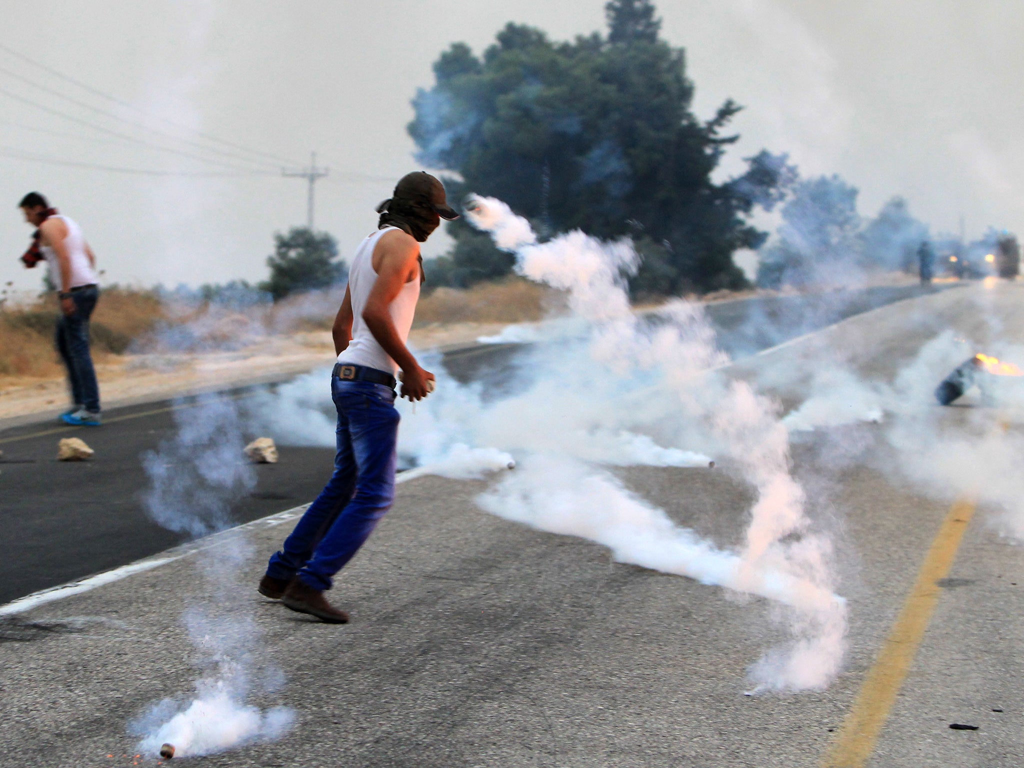 Palestinian protesters stand amid tear gas smoke during clashes with Israeli security forces following a protest in reaction to the death of the toddler