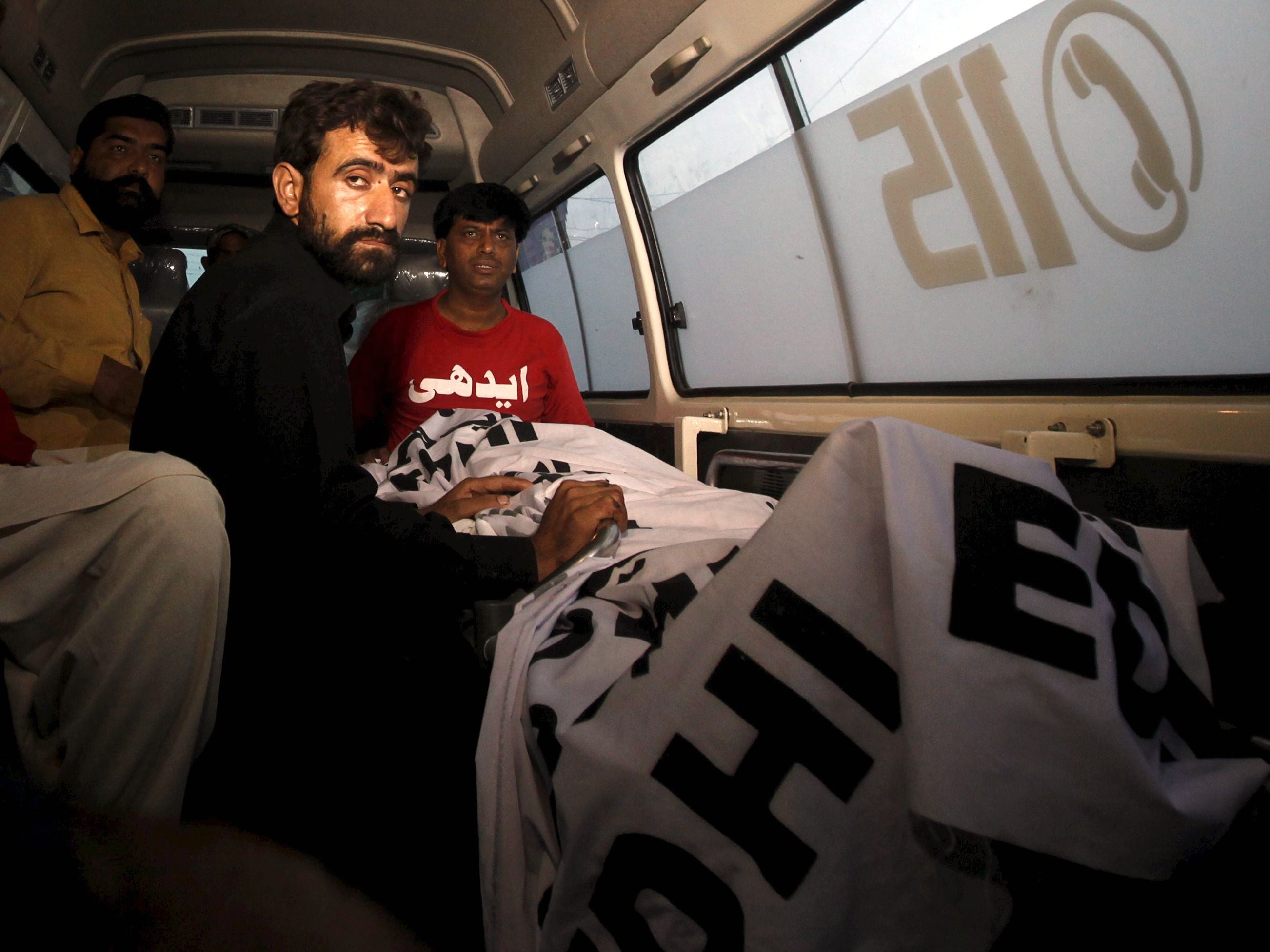 Abdul Majeed sits in an ambulance beside the body of his brother, Shafqat Hussain