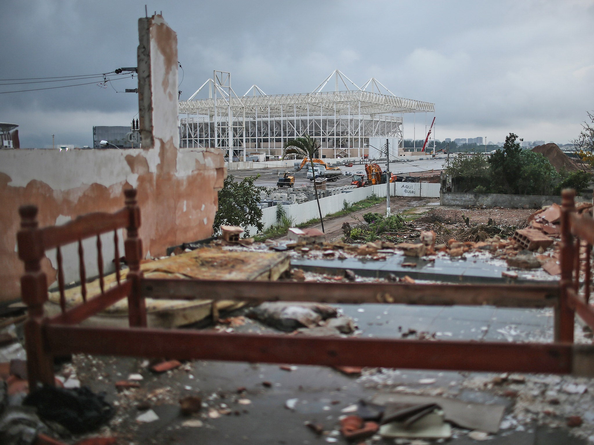 A bedframe remains in a partially demolished home in a Rio favela, with the Olympic Aquatics Stadium construction ongoing in the background (Getty)