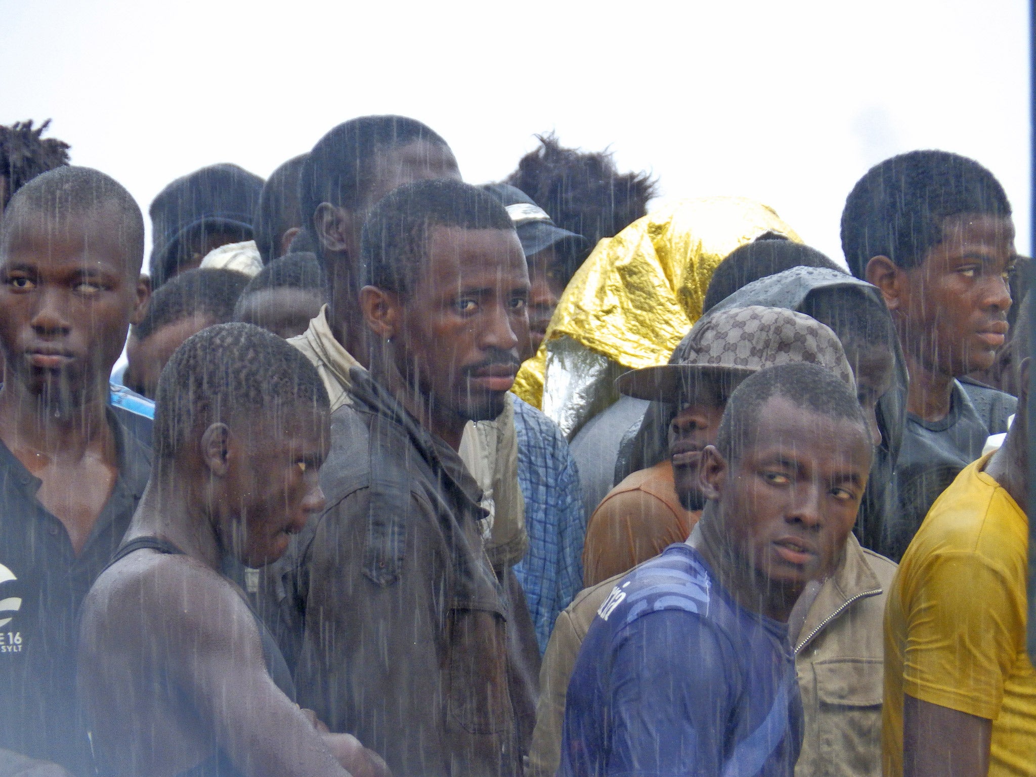 Migrants wait in the rain after disembarking from the coastguard ship in Sicily in August 2015