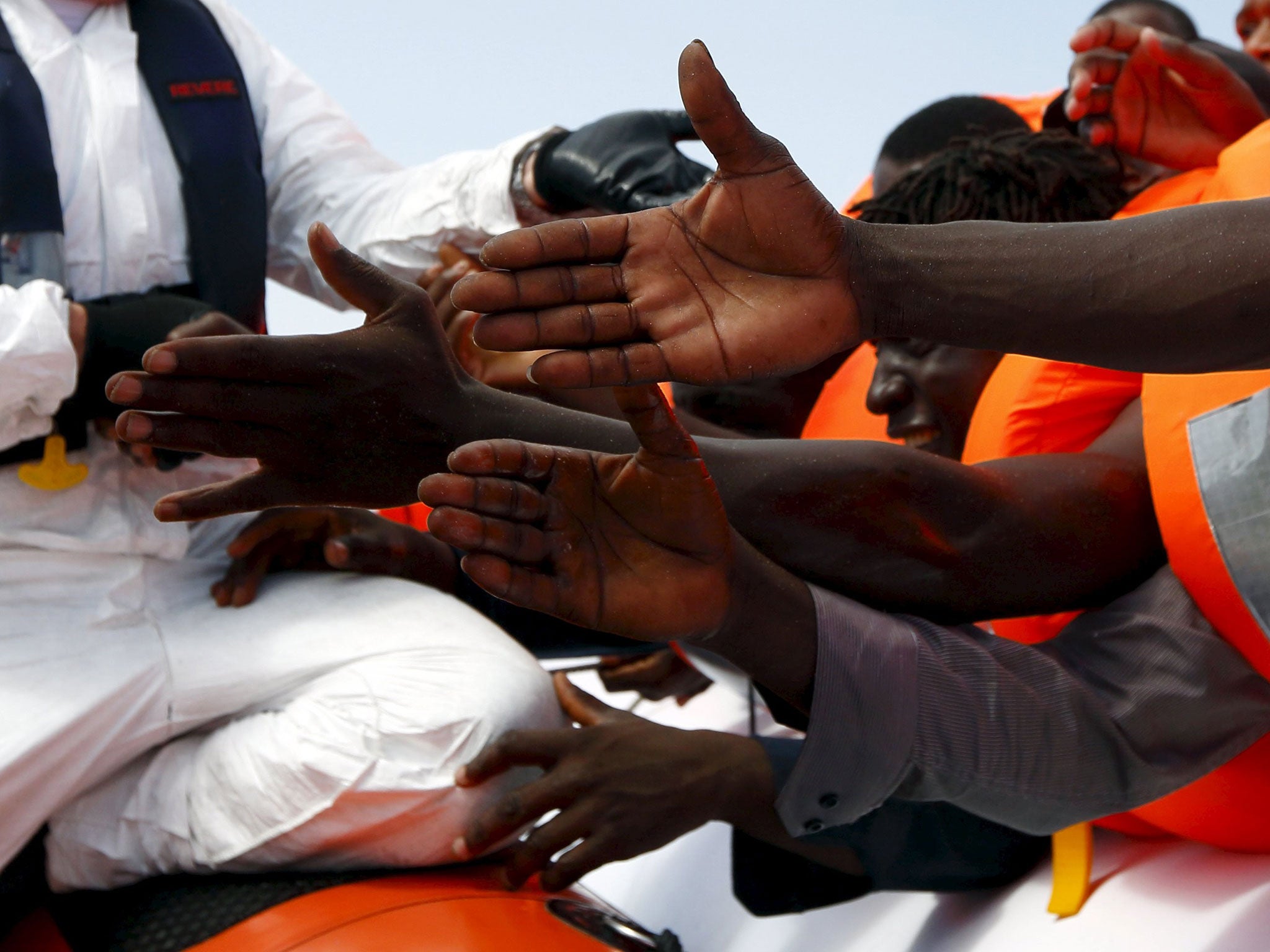 Migrants reach out to grab hold of Migrant Offshore Aid Station (MOAS) rescuers on a RHIB (Rigid-hulled inflatable boat) before being taken to the MOAS ship MV Phoenix some 20 miles (32 kilometres) off the coast of Libya, August 3, 2015