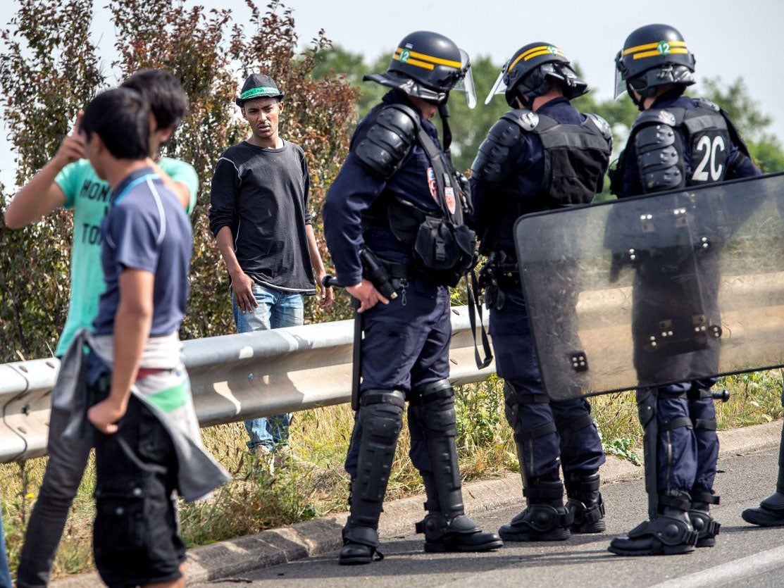 French riot police try to prevent migrants from reaching the road leading to Calais' ferry port
