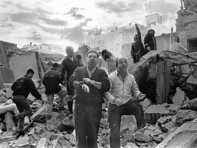 Firemen search as wounded  people walk over the rubble left after a bomb exploded at the Argentinian Israelite Mutual Association (AMIA in Spanish) in Buenos Aires, 18 July 1994.