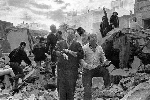 Firemen search as wounded  people walk over the rubble left after a bomb exploded at the Argentinian Israelite Mutual Association (AMIA in Spanish) in Buenos Aires, 18 July 1994.