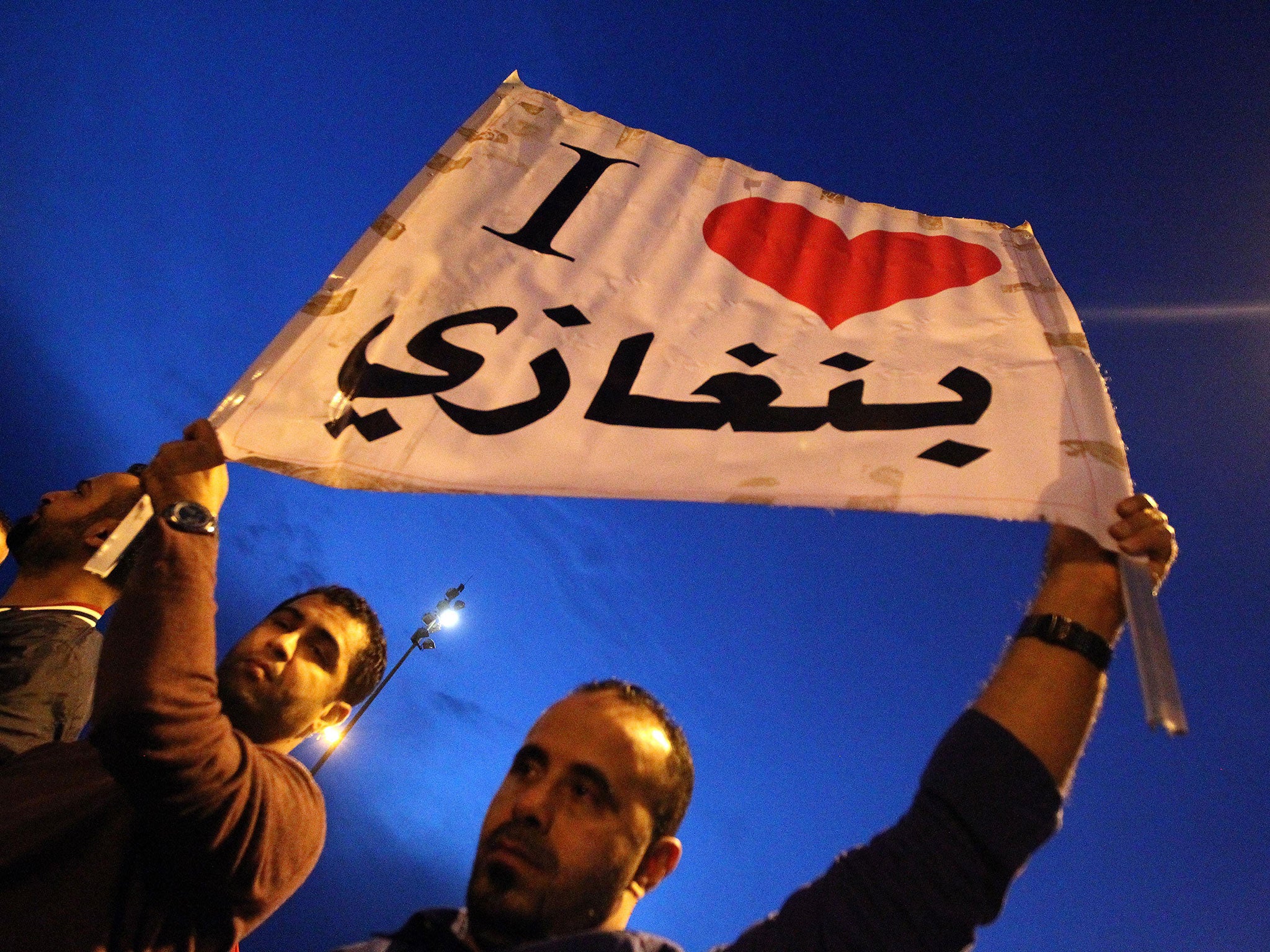 Protesters raise up a placard reading in Arabic "I love Benghazi" during a demonstration in front of the Tibesti hotel in support of the Libyan Army and Police