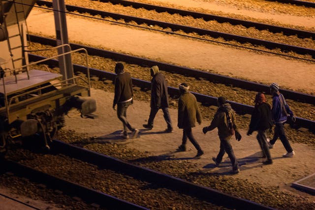 Migrants walk along the train tracks after crossing a fence as they attempt to access the Channel Tunnel in Calais (AP)