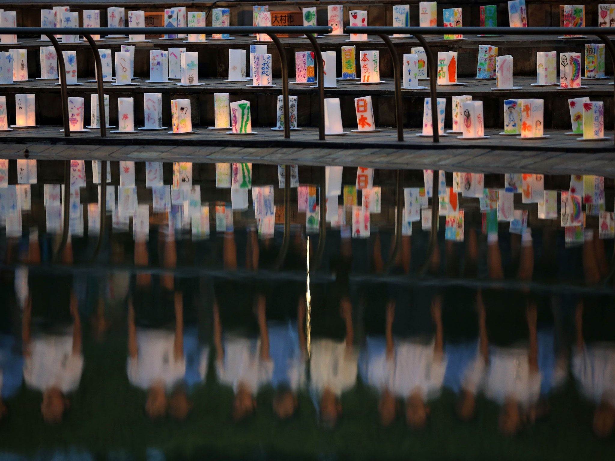 Paper lanterns are placed for the victims of the atomic bombing as students are reflected in a pound on Nagasaki