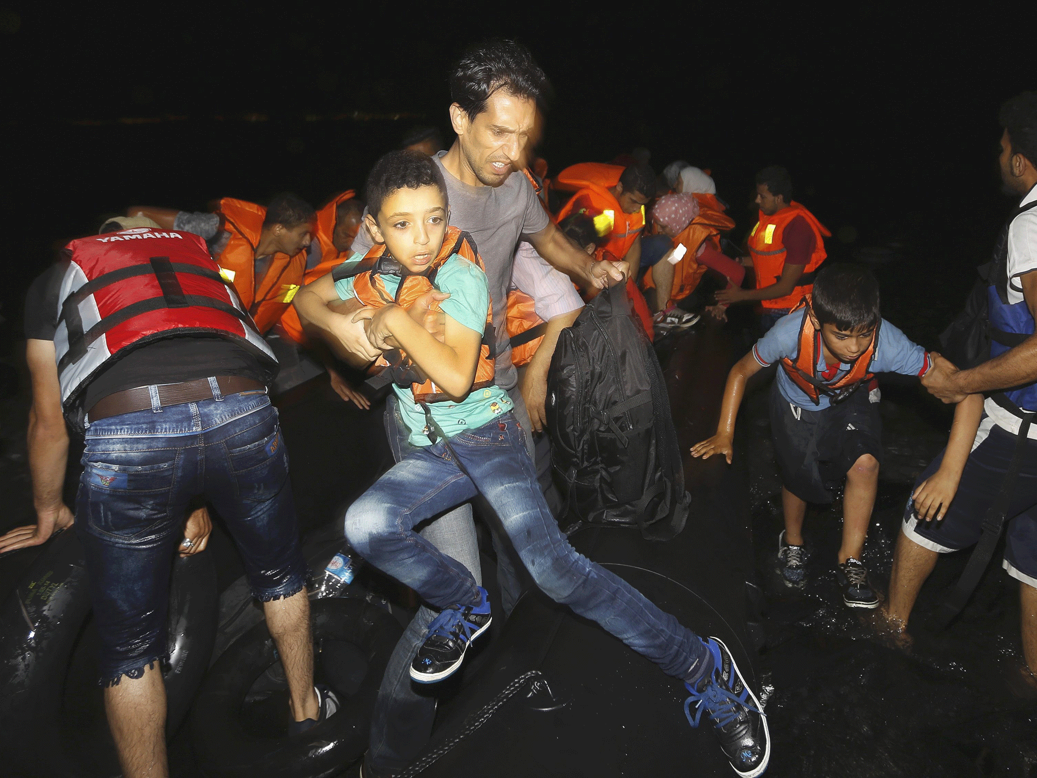 A Syrian refugee strugles to jump off a dinghy while holding his son as they arrive on Kos