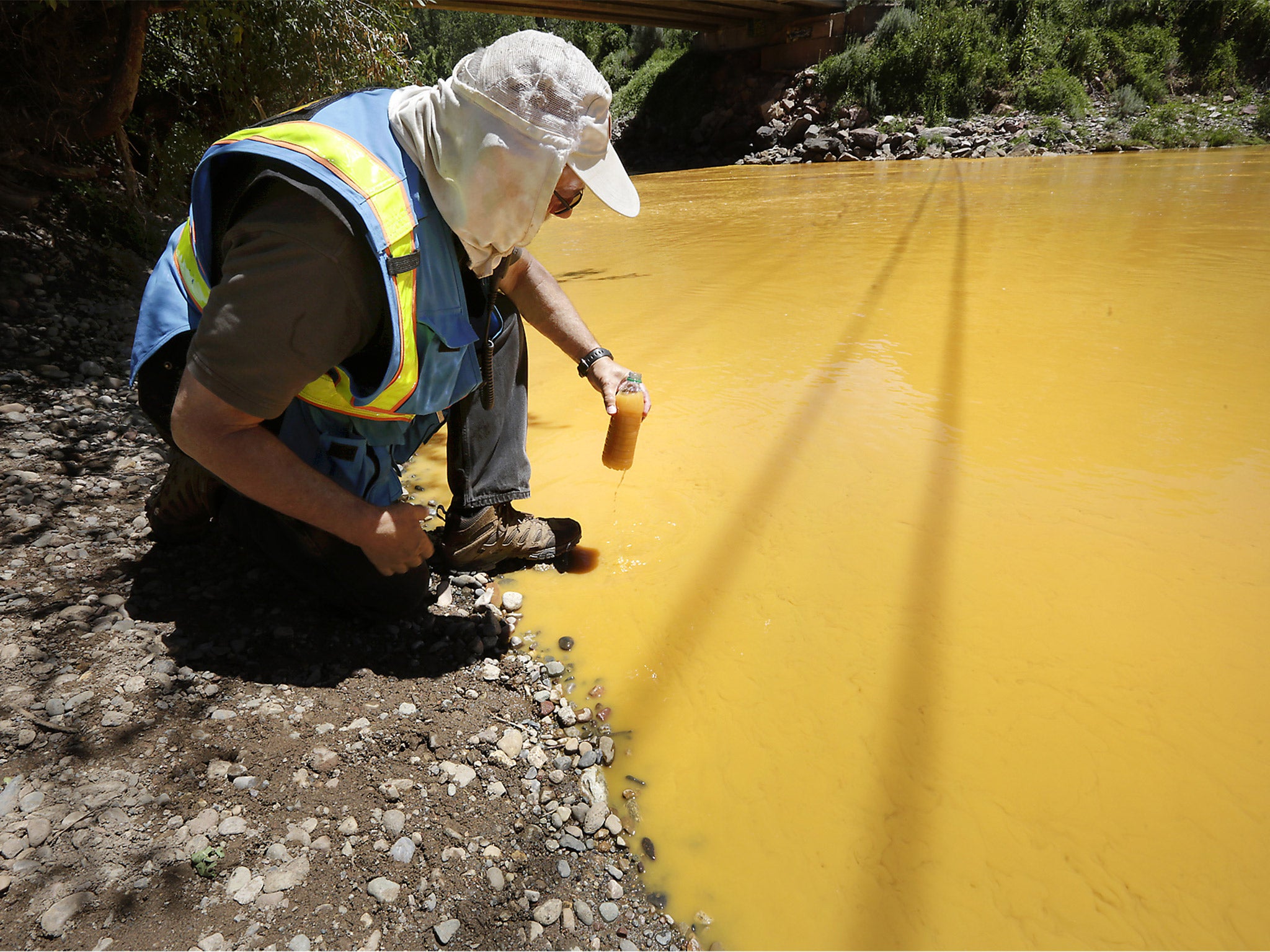 An environmental protection worker takes a sample from the polluted Animas river