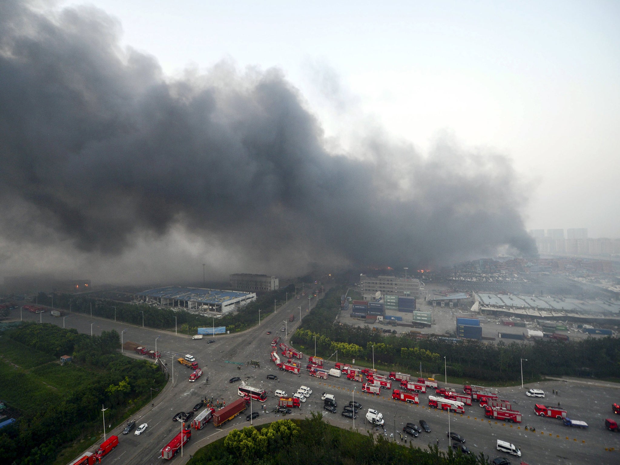 Firefighter's truck and other rescue vehicles are pictured as smoke rises among shipping containers after explosions at Binhai new district in Tianjin