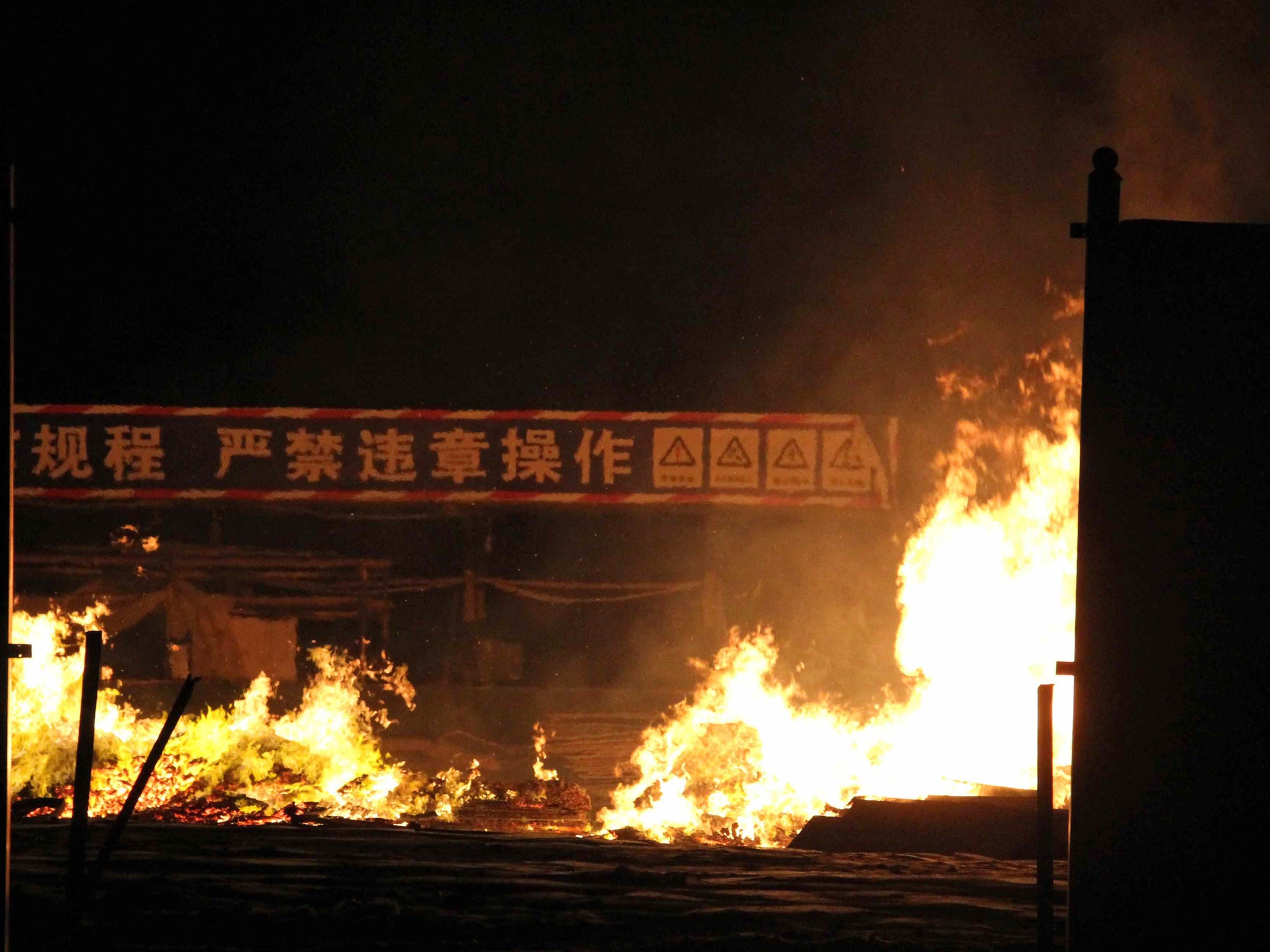 Flames rise as a banner in the background reads "no illegal operations" at the site of a series of explosions in Tianjin, witnesses described a fireball from the blasts ripping through the night sky.