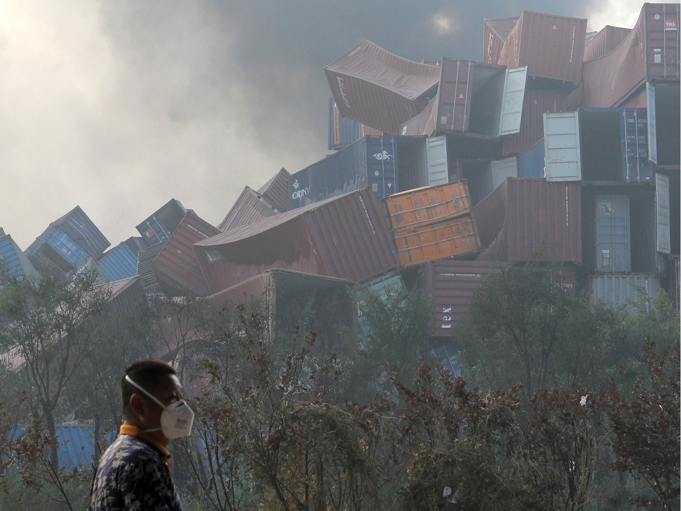 A man wearing a mask walks past overturned shipping containers after explosions hit the Binhai new district in Tianjin.