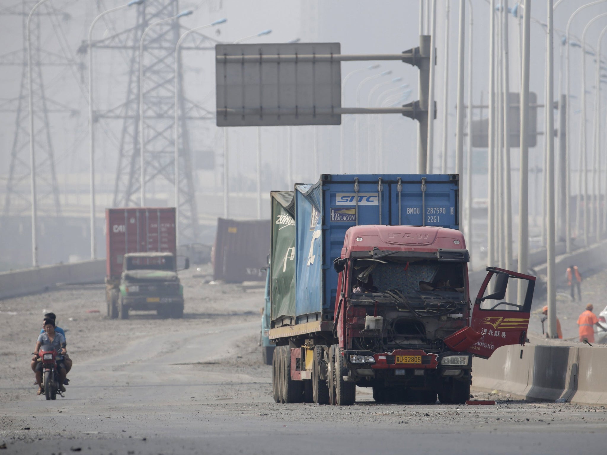 Motorcyclists ride along a highway, next to damaged trucks, near the site of the explosions at the Binhai new district in Tianjin