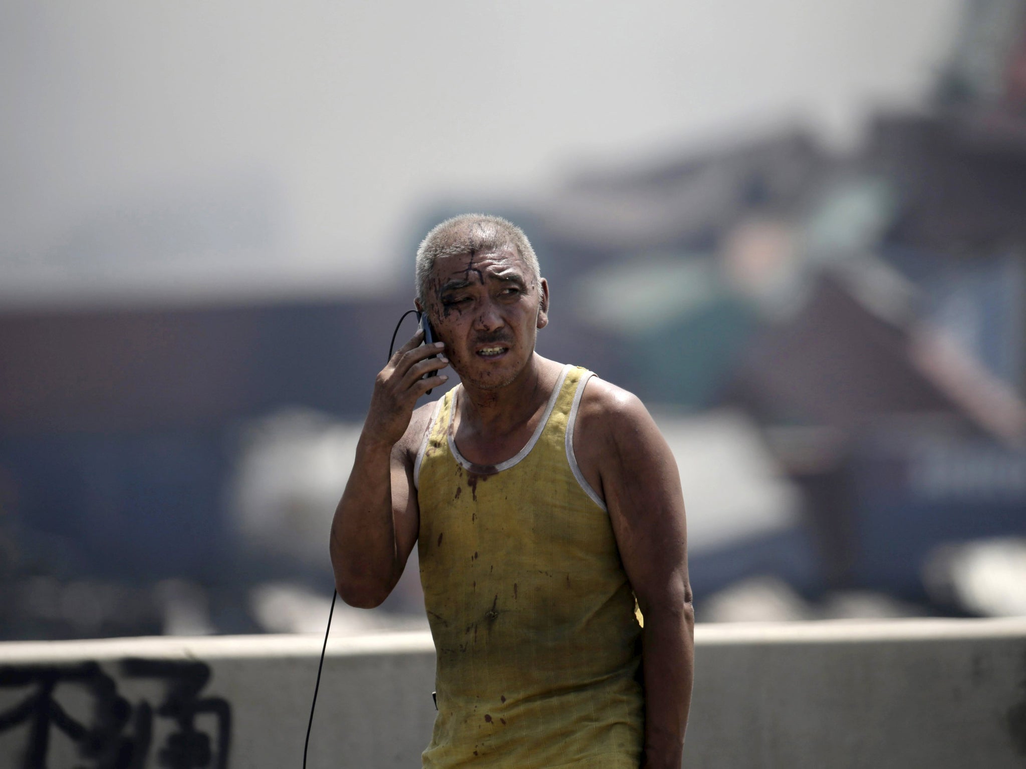 A survivor talk on his mobile phone at the site of the explosions at the Binhai new district in Tianjin