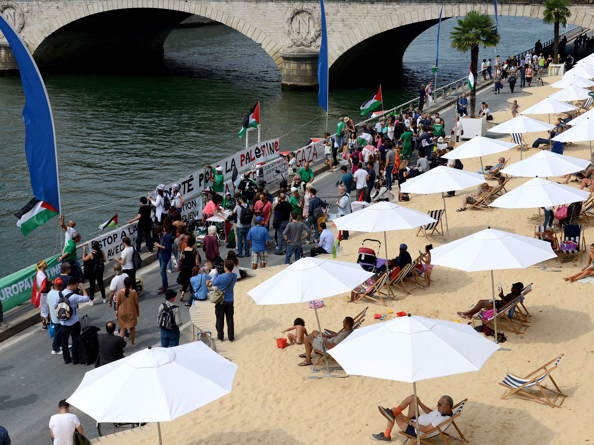 Palestinian supporters hold placards in front of people sunbathing at Tel Aviv sur Seine in Paris