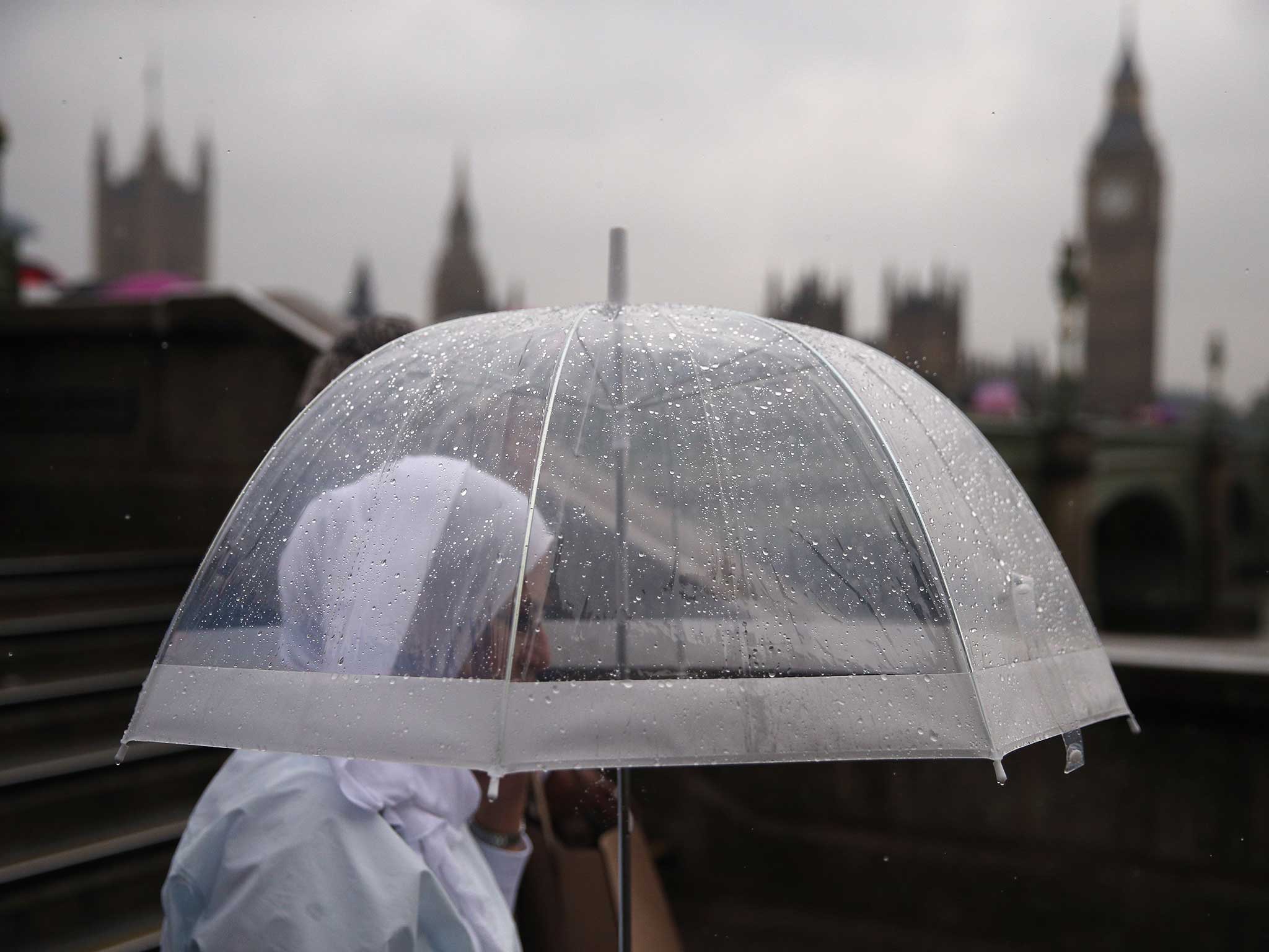 A tourist in London shelters under an umbrella during a downpour