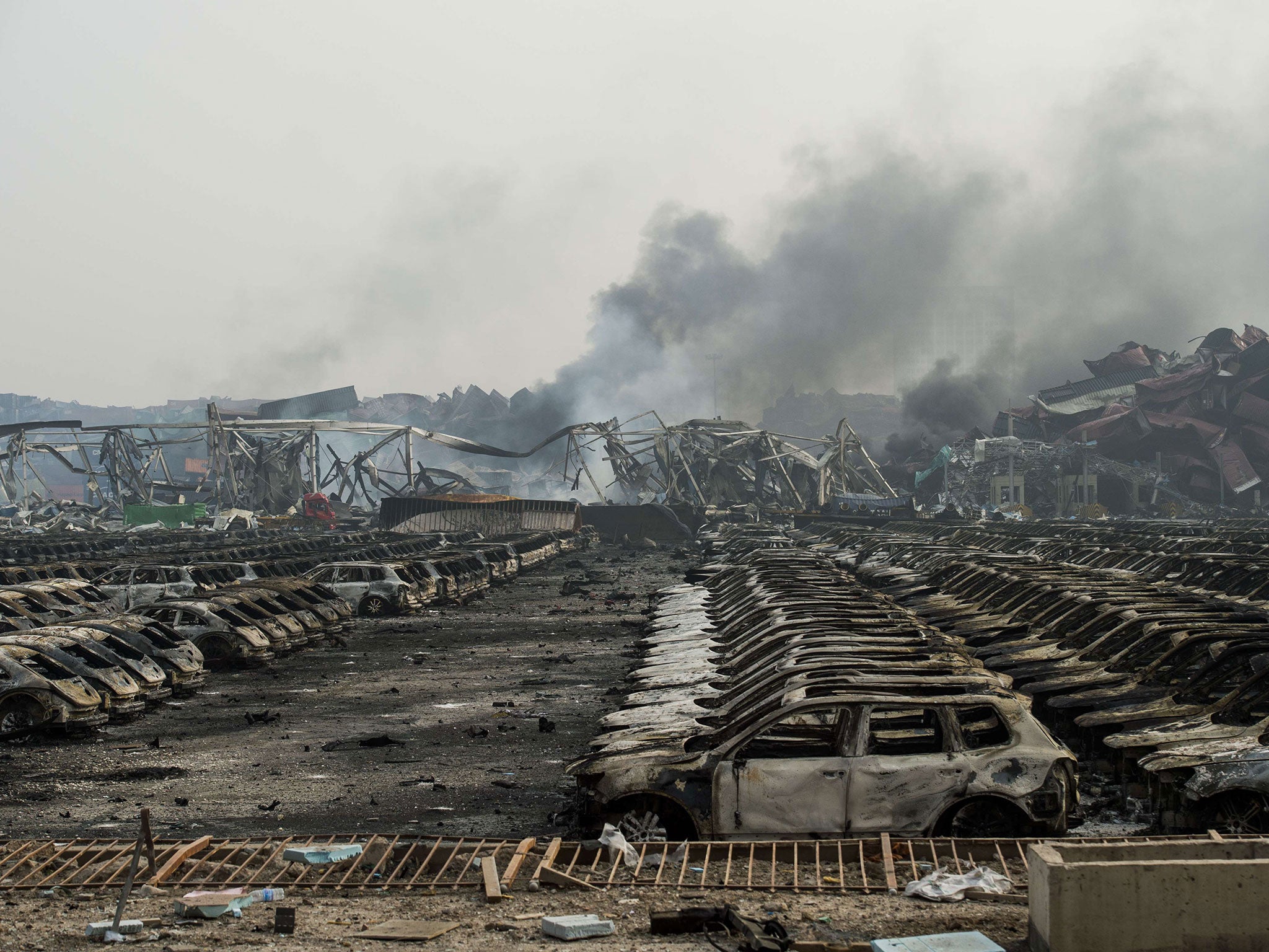 Smoke billows from behind burnt out Volkswagen cars the second morning after a series of explosions at a chemical warehouse hit the city of Tianjin