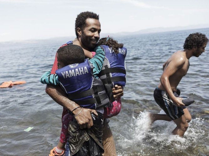 A migrant carries his two children as he gets off of an inflatable boat after arriving on the Greek island of Lesbos