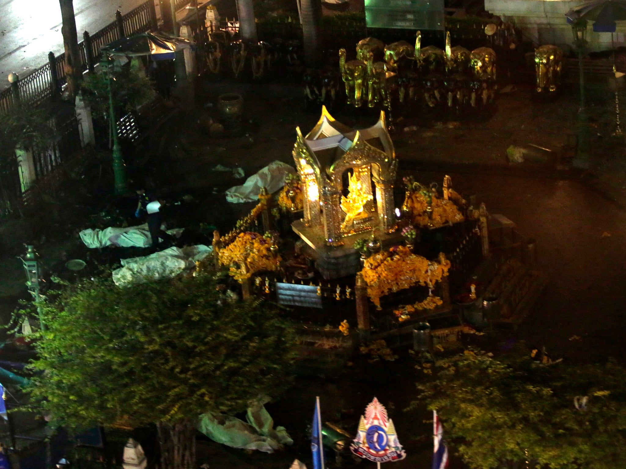 A general view taken from a moving train shows bodies covered in white sheets around the Erawan Shrine -