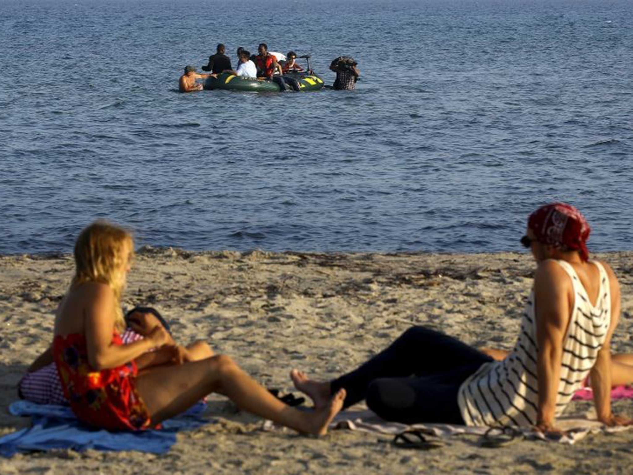 Tourists sunbathe on a beach in Kos as migrants struggle to the shore